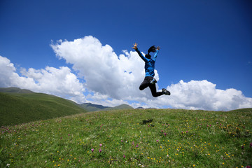 joyfully woman jumping on mountain top grassland