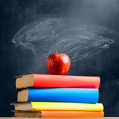 Back to School. Books and fresh apple against chalkboard