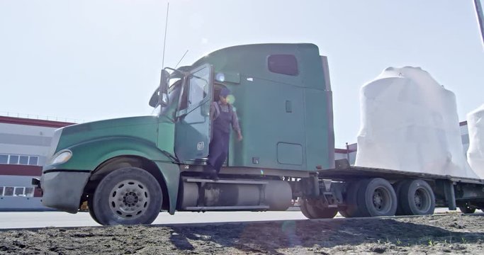 Slow motion of black woman in uniform getting off driver cabin of semi-trailer tractor and walking to factory