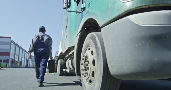 Slow motion rear view of female mechanic walking with tool case along semi-truck to factory