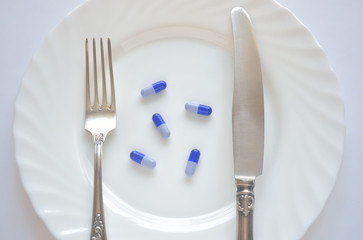 A few blue pills on a porcelain plate with a metal cutlery