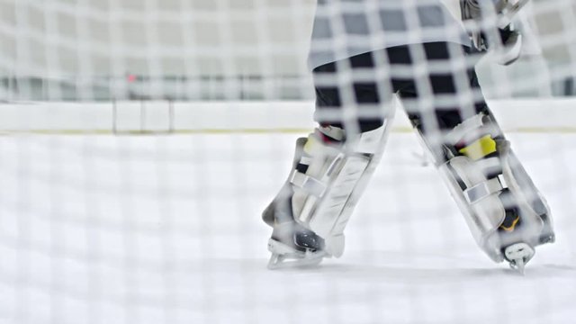 Shot from behind net of ice hockey goaltender guarding net and blocking goal by unrecognizable forward in white uniform