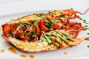 Italian cuisine. Whole lobster baked and sliced in half Served with tomato salad and sauce on white plate