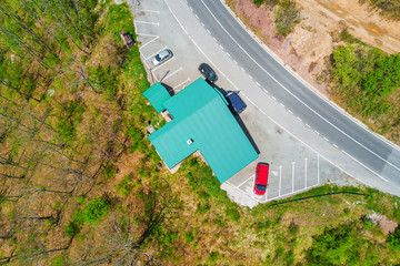 Fototapeta premium Building with a green roof and parked cars on the edge of the road in the forest, top view