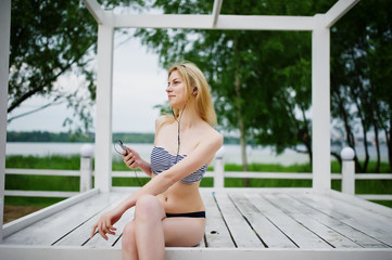 Portrait of a fabulous young woman in bikini sitting and posing on a white wooden gazebo in the...