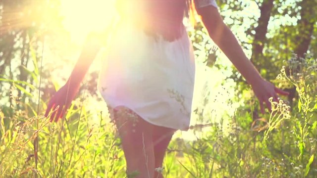 Beauty sexy brunette girl in short white dress walking on field with wildflowers, enjoying nature outdoors. Slow motion 240 fps. 4K UHD video 3840x2160