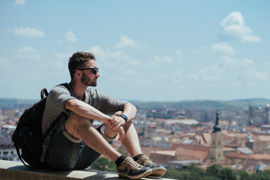 Man traveler with backpack explores the city looking at the panoramic view of the city and the coast. The concept of travel is discovering new places