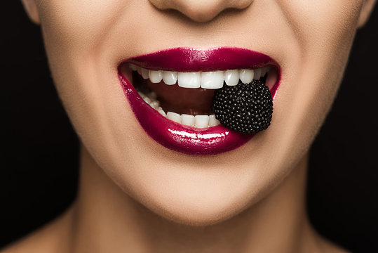 close up view of woman with black jelly candy in mouth, isolated on black