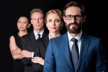 confident middle aged businesspeople standing with crossed arms and looking at camera isolated on black
