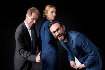 businessman touching buttocks of female colleague while male colleague laughing at camera, sexual harassment at work concept