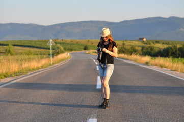 Obraz premium Woman with a camera on the middle of the road in mountains. Forty Years old woman on the road