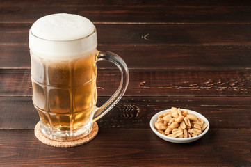 glass of cold frothy lager beer and peanuts plate on wooden table