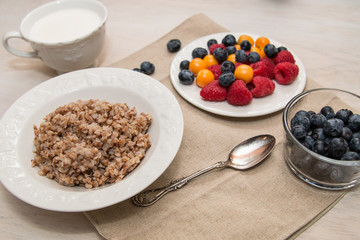 Buckwheat breakfast with berries on white plate, blueberry, golden berry, physalis, raspberry, milk