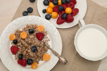 Buckwheat breakfast with berries on white plate, blueberry, golden berry, physalis, raspberry, milk