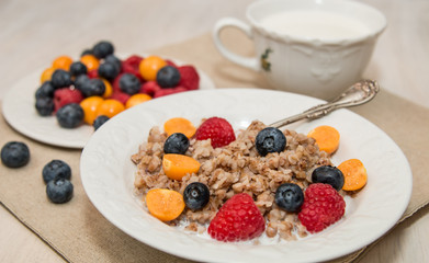 Buckwheat breakfast with berries on white plate, blueberry, golden berry, physalis, raspberry, milk