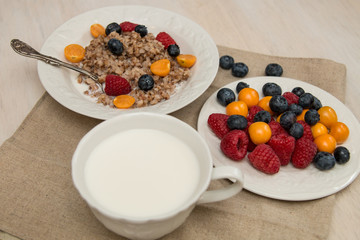 Buckwheat breakfast with berries on white plate, blueberry, golden berry, physalis, raspberry, milk