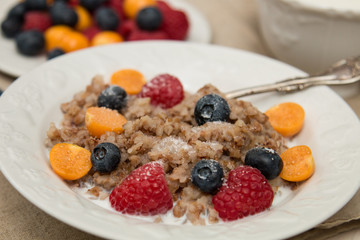 Buckwheat breakfast meal with berries on white plate, milk, blueberry, golden berry, physalis, raspberry 