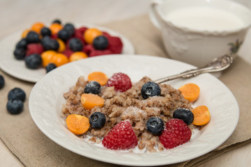 Buckwheat breakfast with berries on white plate, blueberry, golden berry, physalis, raspberry, milk