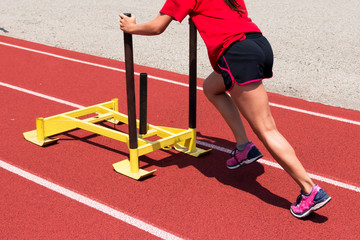 Female pushes a yellow sled on a track at practice