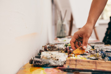 Artist hand picking up color tubes from the table