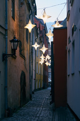 Narrow street lit by streetlights in the form of stars in the old town in Riga