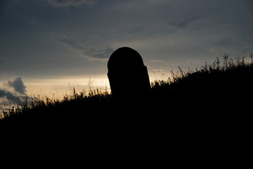 silhouette of lonely graveyard stone on hill at sunset