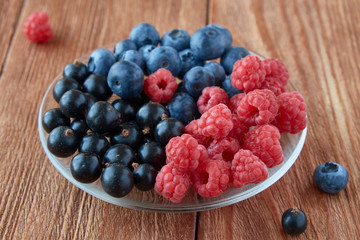 Delicious, fresh berries. Black currant, raspberry, blueberries on a wooden background.