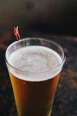 miniature people stand on glass of beer 