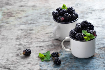 Fresh blackberries with mint leaves in a white cup on a rustic wooden background with copy space.
