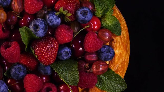 Tasty homemade pie with mixed berries and mint leaves on black background. 4K closeup rotation. Top view.
