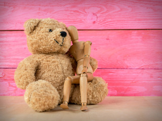 Wooden puppet with a teddy bear and a pink wooden background.