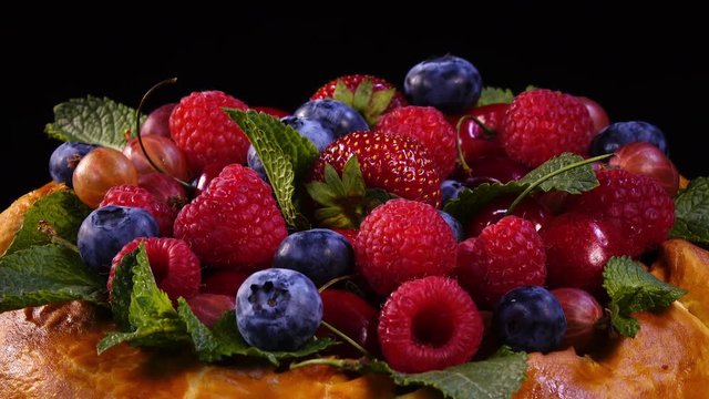 Mixed berries and mint leaves on beautiful homemade tasty pie. Close up rotation against black background. 4K.
