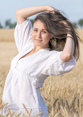 Beautiful young sexy woman playing with her long hair in golden wheat field at summer sunny day