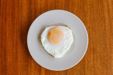 Fried egg in white plate on wooden table.