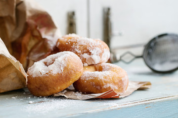 Homemade donuts with sugar powder from paper bag served with vintage sieve on blue wooden table....