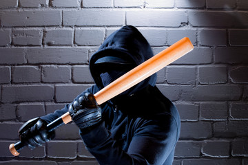 An aggressive man with a baseball bat stands in front of a wall