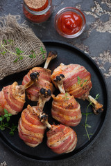 Oven-baked chicken legs wrapped in bacon served on a metal plate, vertical shot, view from above
