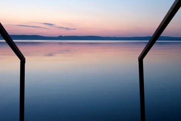 purple sunset at Balaton lake in summer assimetric railing leads in the water - thin clouds, velvet sky and hills in background