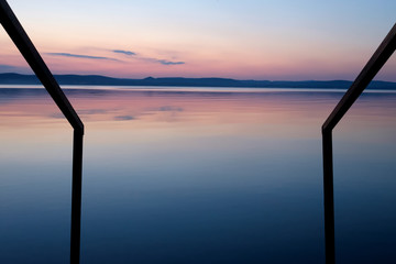 purple sunset at Balaton lake in summer railing leads in the water - thin clouds, velvet sky and hills in background