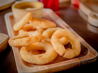 Fried breaded onion rings with sauce on a classic wooden plate.