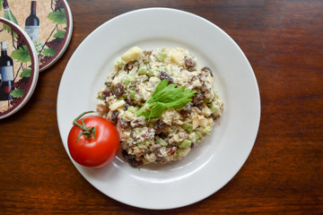 Chicken salad on white plate with tomato on dark wood background