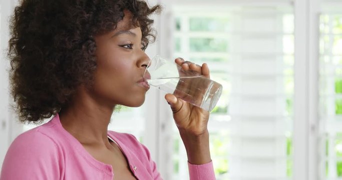 African American woman drinking glass of water and smiling