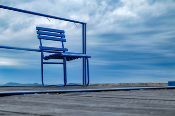 blue metal chair on wooden pier at Balaton lake - lonely day, windy and cloudy weather in the summer season, bottom perspective