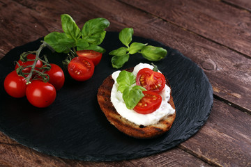 Bread with cream cheese and tomato for lunch table. Sharing antipasti on party or summer picnic time over wooden rustic background.