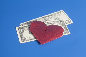 Red paper heart origami and dollar bills on blue background