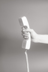 Hand holding white telephone tube on gray background.