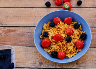 Corn flakes on a strawberry and blackberry on a plate.