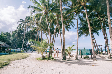 Young couple look to the sea,the fresh green palm trees around. They stand on the white sand with a...