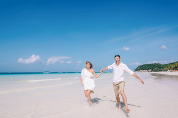 Active couple having fun and running on a white sandy beach with blue sky and turquois water on the background. Men and women are happy and laughing together