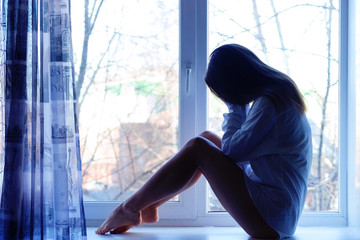 Cute sad girl near window at home